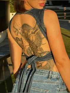 a woman with tattoos on her back standing next to a bench