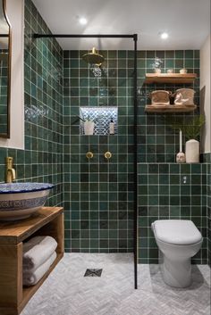 a green tiled bathroom with shelves above the toilet