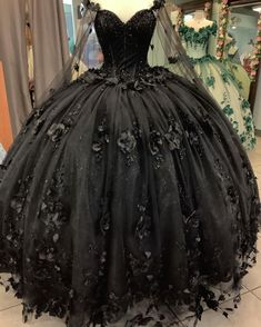 Step into your Quinceanera with elegance and mystery in this stunning black ball gown. This dress is crafted from luxurious tulle and features a dramatic ball gown silhouette with a chapel train that adds a royal finish to your look. The sweetheart neckline and long sleeves exude sophistication, while the intricate beading and appliqued floral details bring a soft yet bold charm to the ensemble. A corset back ensures a perfectly sculpted fit, making this dress as comfortable as it is enchanting. Quinceanera Dresses With Flowers, Black Quince Dress, Long Sweet 16 Dresses, Lavender Prom Dress Long, Dresses With Flowers, Black Quinceanera, Quinceanera Dresses Black, Cheap Quinceanera Dresses, Black Quinceanera Dresses