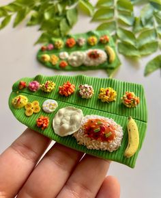 a hand holding a miniature food tray with rice and fruit on it's side