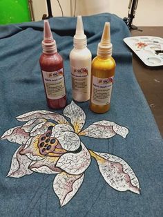 three bottles of paint sitting on top of a blue table cloth next to each other