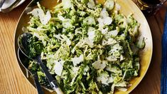 a bowl filled with broccoli and cheese on top of a wooden table next to utensils