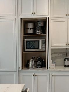 a kitchen with white cupboards and appliances in the cabinets, including coffee maker, toaster oven, tea kettle, and other items