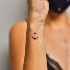 a woman with a small anchor tattoo on her left wrist and hand behind her ear