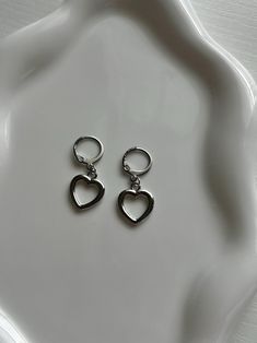 A simplistic earrings pair made with silver heart charms. Subtle enough to wear for the rainiest days, and elegant enough to dress up. Includes 1 pair of earrings (2 hoops). Trendy Sterling Silver Heart Earrings For Everyday, Trendy Everyday Heart Dangle Earrings, Trendy Silver Hoop Earrings With Heart Charm, Trendy Silver Single Heart Earring, Trendy Nickel-free Metal Heart Earrings, Trendy Heart-shaped Nickel-free Hoop Earrings, Trendy Silver Heart Charm Earrings, Trendy Silver Hypoallergenic Heart Earrings, Trendy Silver Heart Hoop Earrings