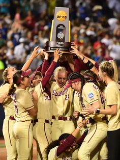 a group of women's baseball players holding up a trophy on top of each other