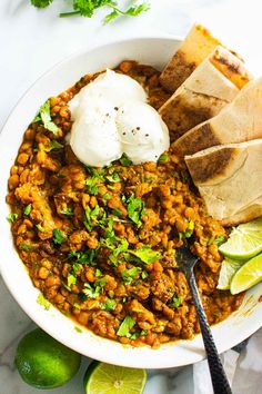 a white bowl filled with beans and tortillas next to sliced lime wedges