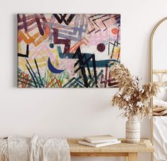 an abstract painting hangs on the wall above a wooden table with a plant in it