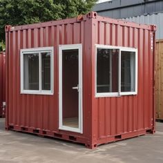 a red shipping container sitting on top of a parking lot next to other containers and trees