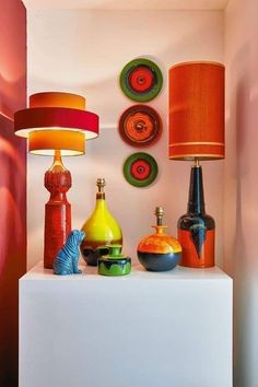 a white shelf topped with lots of colorful vases and lamps