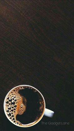 a cup of coffee sitting on top of a wooden table next to a cell phone