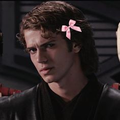 a young man with a pink bow in his hair looking at the camera while standing next to an alien