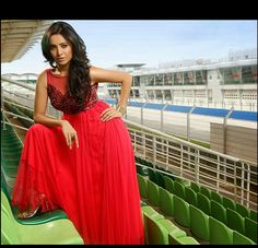 a woman in a long red dress sitting on the bleachers at a stadium