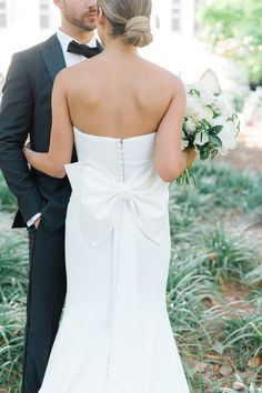 a bride and groom standing together in the grass