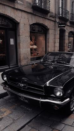 an old black mustang parked on the side of the road in front of a building