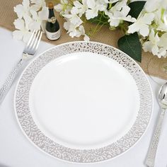 a white table setting with silverware, flowers and wine bottle on the tablecloth