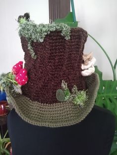 a crocheted hat with flowers and leaves on the top, sitting on a mannequin head