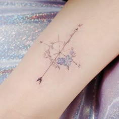 an arrow and flowers tattoo on the right side of the left arm, with blue flowers in the middle