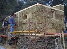 two men working on a building made out of hay bales and wood sticks with scaffolding around it