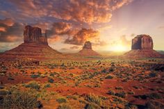 the sun is setting over monument buttes in arizona, with red dirt and green grass