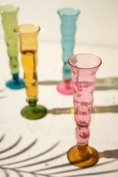 four different colored glass vases sitting on top of a white table with shadows coming from them