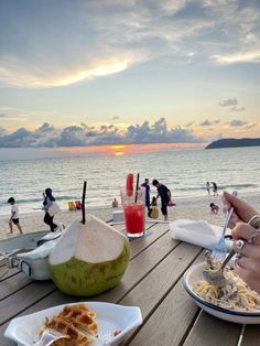 two plates of food on a wooden table at the beach with people in the background