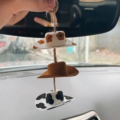 a car dashboard with a cow decoration hanging from it's side mirror, and someone holding their hand up to the rear view mirror