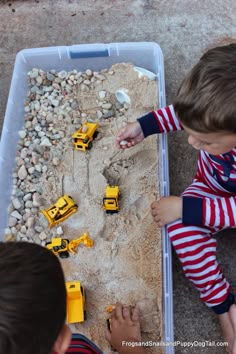 two young boys playing with construction vehicles in the sand