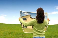 a woman standing in a field holding up an image of a house