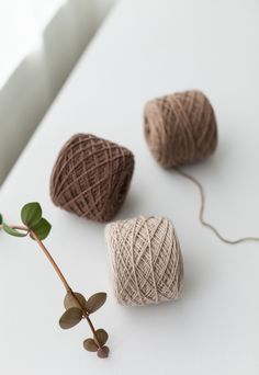 three balls of yarn sitting on top of a white table next to a green plant