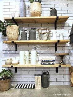 the shelves are filled with pots, mugs and other decorative items on display in front of a white brick wall