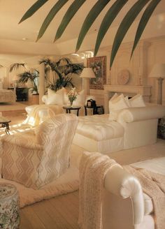 a living room filled with white furniture and lots of palm leaves on top of it