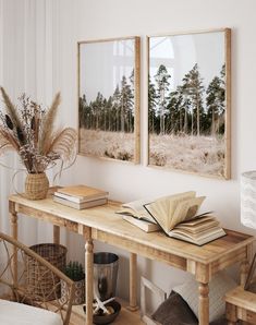 two framed photographs hang on the wall above a wooden table with books and vases