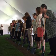 a group of people holding shovels standing next to each other in front of a tent