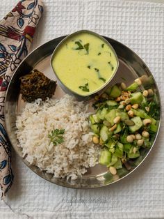 a metal plate topped with rice and veggies next to a bowl of sauce