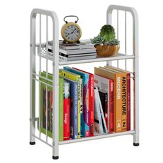 a white book shelf with books and a clock on the top, sitting next to a potted plant