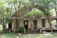 an old run down house with a stop sign on the front porch and trees surrounding it