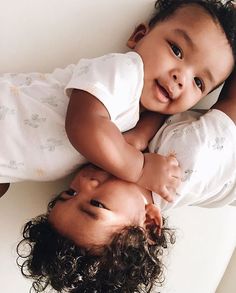 two children laying on top of each other with their arms around the baby's head