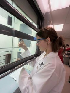 a woman in white lab coat looking out window at something on the other side of her