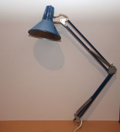 a blue desk lamp sitting on top of a wooden table next to a white wall