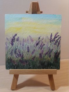 an easel with a painting on top of it that has purple flowers in the grass