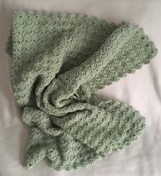 a green crocheted blanket laying on top of a white bed sheet with a knoted edge