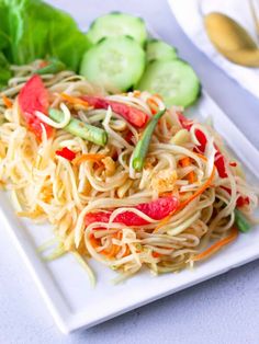 a white plate topped with noodles and veggies next to cucumber slices