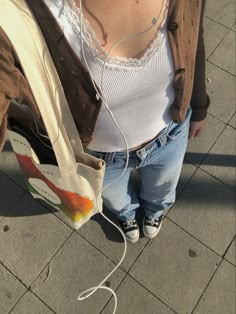 a woman is standing on the sidewalk with headphones in her ears and holding a shopping bag