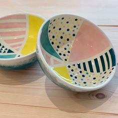 two colorful bowls sitting on top of a wooden table with polka dots and lines painted on them