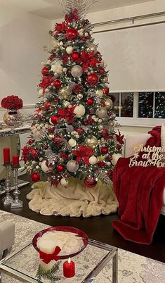 a christmas tree decorated with red and silver ornaments in a living room setting, surrounded by holiday decorations