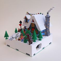 a toy house made out of legos on a white surface with trees and snow