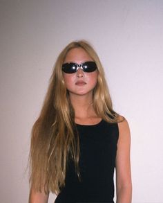 a woman with sunglasses on her face and long blonde hair standing in front of a white wall