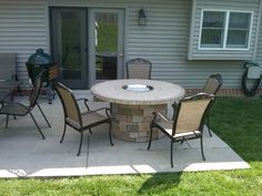 an outdoor table with chairs around it on a patio next to a building and grass