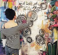 a woman is writing on a wall covered in graffiti and flowers, with her hands behind her back to the camera